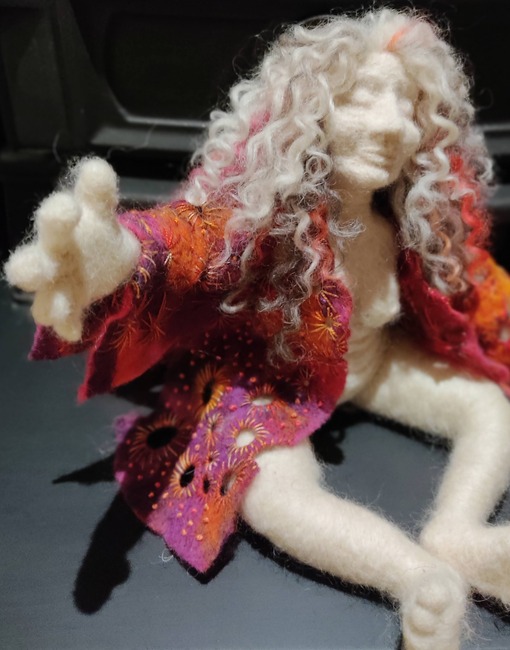needlefelted artdoll of a charismatic woman, her arms outstretched. She wears a jewel colour coat with rich embroidery.
