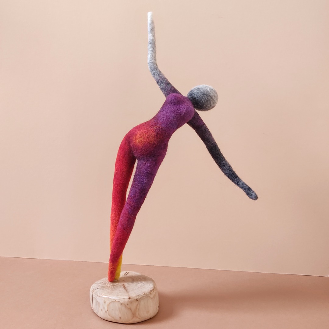 a long tall dancer reaches her arms in joy. She is worked in flame coloured needlefelted wool