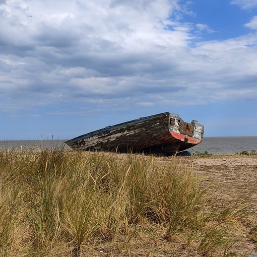 image of an old fishing boat at the top of the shore, by some coastal grasses
